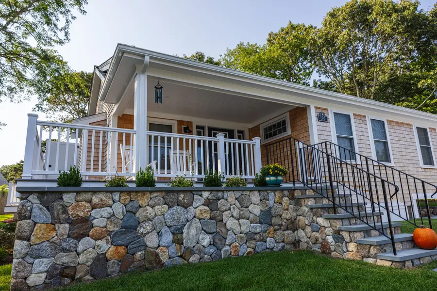 Shingled cottage with a white porch on a fieldstone base