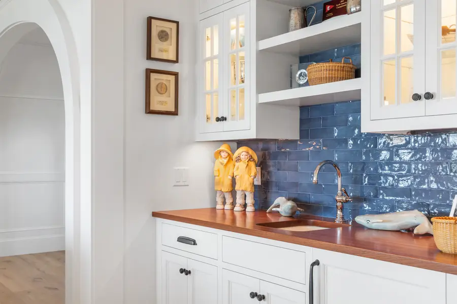 Wet bar with blue tile backsplash, wood counter and glass-front cabinets