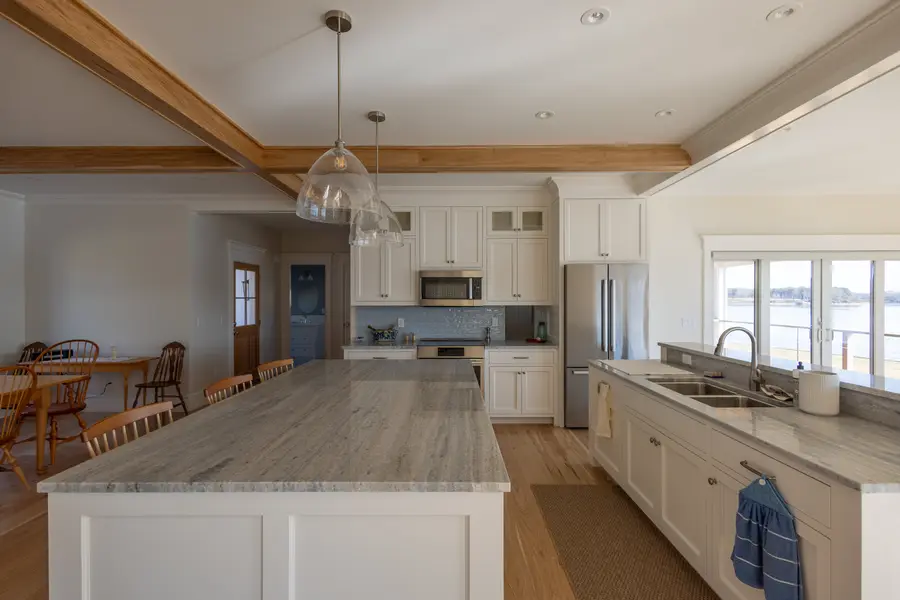 White kitchen with a large stone-top island, glass pendants and wide-plank oak floors