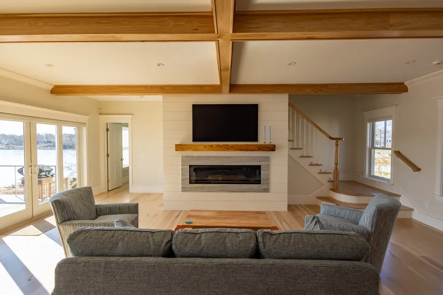 Living room under a beamed ceiling, with a linear fireplace and windows on the river